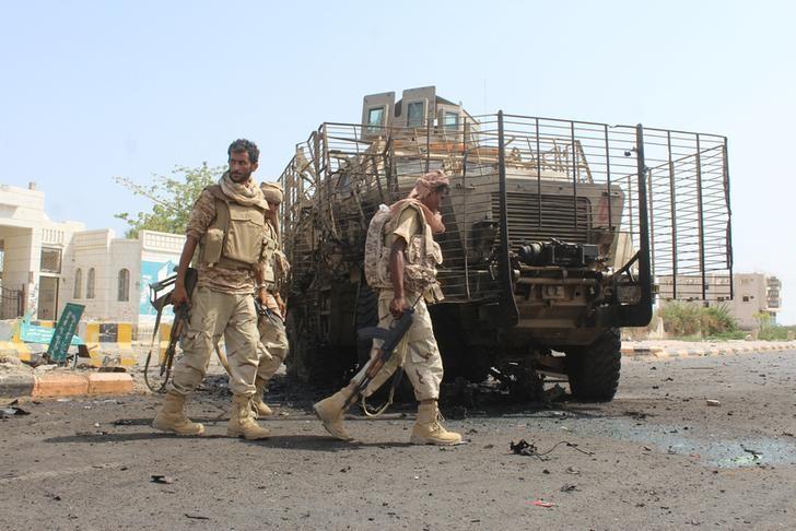 Yemeni army soldiers walk past a damaged armoured personnel carrier in Yemen's southern city of Zinjibar after army forces took it over from militants August 14, 2016. REUTERS/Stringer/Files